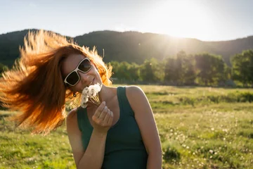 Redhead woman having fun in nature on a warm summer evening. Green mountains and the blue sky in the background. © smallredgirl