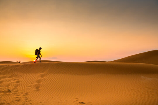 Man photographer with camera and backpack walks on the sand dune at sunset. Yellow sand of the dunes in the desert.