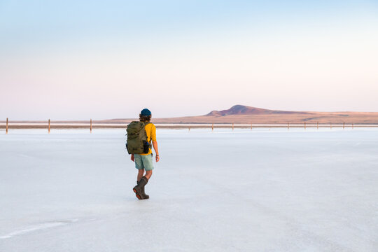 Man traveler with backpack walking on the salt lake at sunset. Salt industry on Baskunchak lake, Russia.