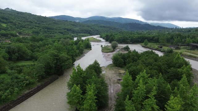 Bird's-eye aerial footage flying downstream over the Tekhuri river near Martvili, Georgia, past a forested island and dense forest on both banks, with forested mountains on the horizon.