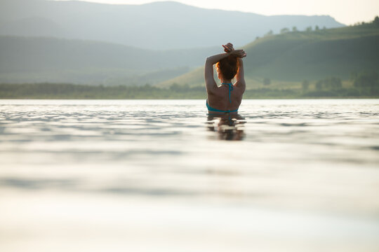 Woman swims in the lake at sunset and enjoying the view of the mountains. Concept of a healthy lifestyle and relaxation in nature