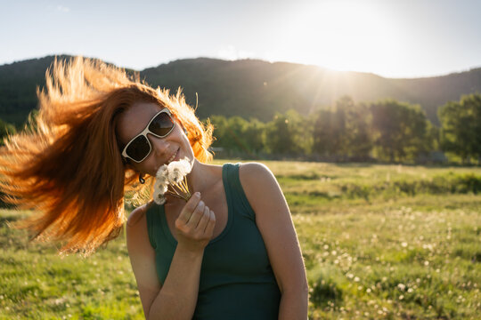 Redhead woman having fun in nature on a warm summer evening. Green mountains and the blue sky in the background.