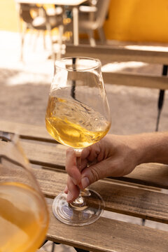 hand swirling natural wine in a glass on a wood table on a narrow picturesque street in europe