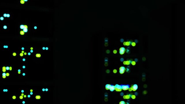 Lights blink from computer servers in a dark room. The scene shows rows of servers connected to each other. The focus is on the glowing lights that indicate server activity