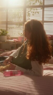 Vertical video of Caucasian teenage girl lying on bed, eating popcorn and looking away. Footage is suitable for streaming platform promos or youth lifestyle commercials