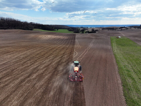 Aerial view of a tractor plowing a large field near Wriezener Alte Oder with brown soil and green grass under a cloudy sky in Brandenburg, Germany.