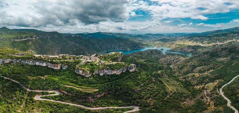 Aerial panoramic view of Siurana village and Siurana Reservoir surrounded by dramatic cliffs, winding mountain roads and rugged landscapes