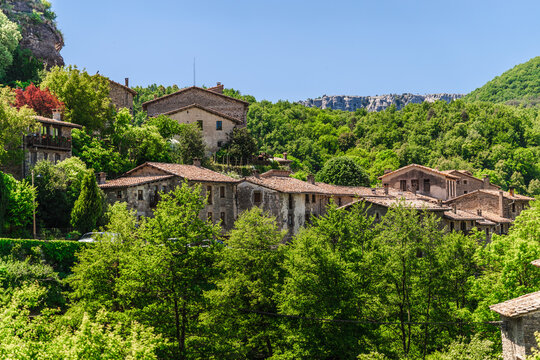 Panoramic view of Rupit village in Catalonia, Spain, featuring historic stone houses nestled among dense green forests and rocky hills