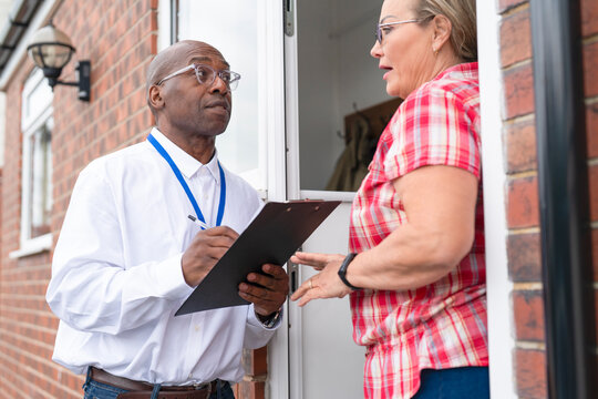 Professional man with a clipboard talking to senior woman outside their house. Concept of home inspection, property assessment, maintenance and professional consultation.