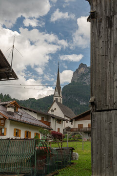 Alleghe, Italy. Alpine village church framed by historic wooden buildings and dramatic Dolomite mountains