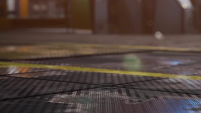 In a spacious industrial area, the camera captures a close view of the textured floor. Yellow lines mark sections of the ground. Light streams in from above, highlighting the surface details.