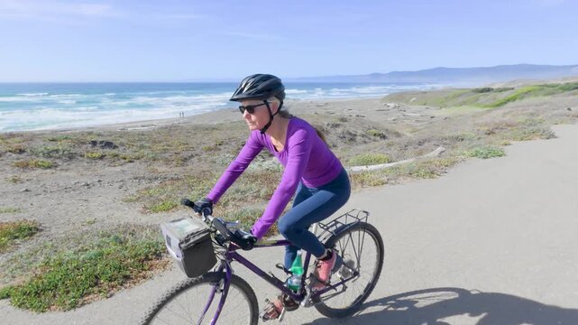 Mature woman enjoys biking on a trail along the ocean in Fort Bragg, California. She rides and explores the beautiful area by the coast.