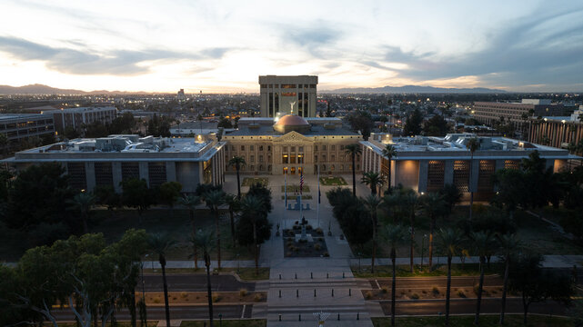 Aerial view of Arizona State Capitol building at sunset, featuring its iconic copper dome, surrounded by palm trees and urban landscape in Phoenix, Arizona, United States.