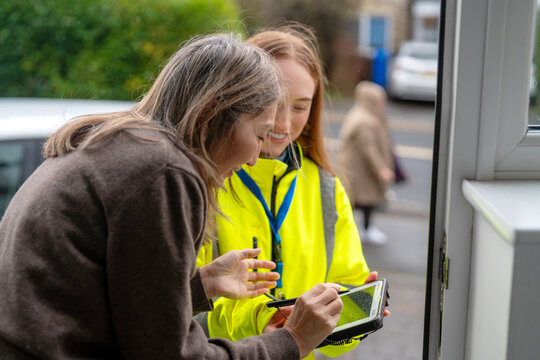 Older woman and young delivery worker interact outside a house while using a tablet