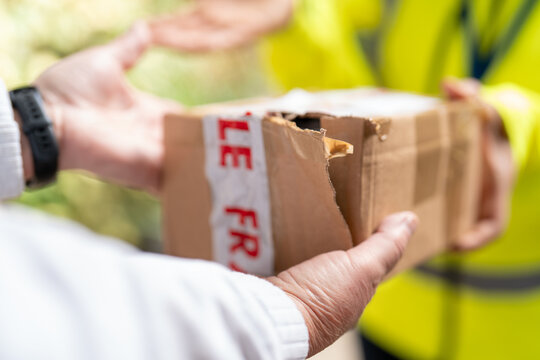 Delivery person holding a damaged package torn parcel was damaged during delivery, illustrating poor delivery service, shipping problems and customer service issues.
