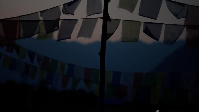 Layered rows of traditional prayer flags hanging low against a deep blue dusk sky in a peaceful rural mountain setting in Nepal