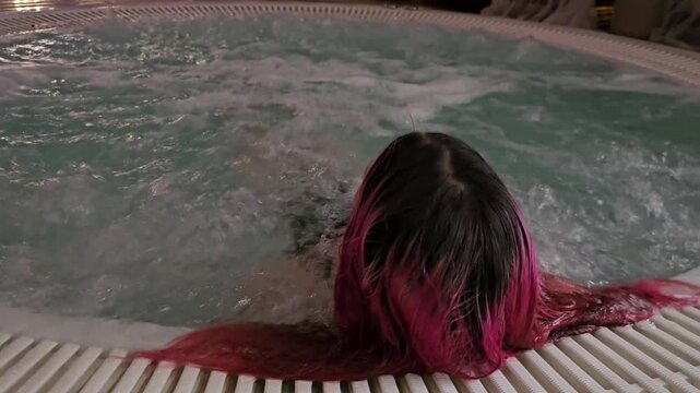 Relaxing in a hot tub at night with colorful hair under dim lights in a cozy setting