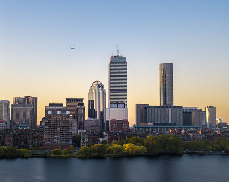 Aerial view of the Boston skyline featuring the Prudential Center and skyscrapers along the Charles River at sunset, with trees lining the riverbank in Boston, Massachusetts, United States.