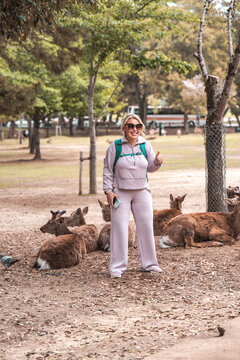 Tourist woman does a cheesy pose in front of wild deer in Nara Japan