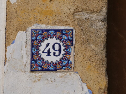 Decorative ceramic house number tile with a blue floral pattern showing the number 49 on a rustic plaster wall.