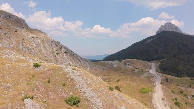 Drone Aerial View Flying Along Mountain Ridge with Winding Dirt Road and Sharp Rocky Peak on Visocica