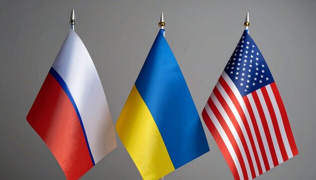 Flags representing various nations stand side by side in a row against a neutral grey background wall.