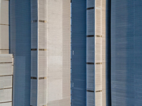 Aerial view of industrial metal silos with vertical ribbed textures and geometric shadows in Banyumas Regency, Central Java, Indonesia.