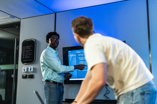 African male developer provides personalized technical guidance and code explanation using AI documentation tools, demonstrating expertise and knowledge transfer in development environment.