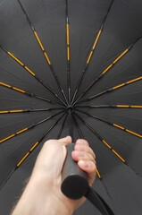 Hand holding black umbrella with orange accents, low angle view from below © DmitryDolgikh