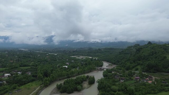 Aerial 4K drone footage flying upstream along the Tekhuri river and over Martvili village in Western Georgia. Overcast sky with dark grey clouds after rain.