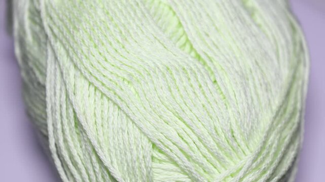 A green ball of yarn lies on a white surface, awaiting use for knitting or crafting. Rotating in a circle