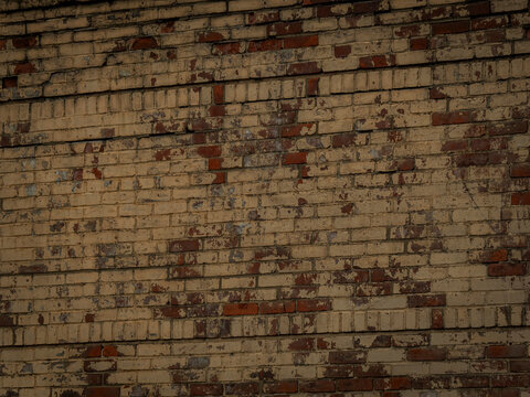 A weathered and aged brick wall texture with peeling tan and beige paint showing red brick beneath in an urban design