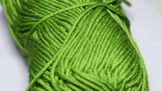 A green ball of yarn sits on a white surface, ideal for use in craft or design projects. Rotating in a circle