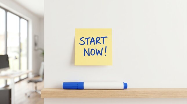 Yellow sticky note with 'START NOW!' written in blue on a white wall with a marker