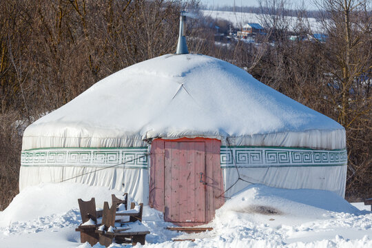 Snow blankets a traditional yurt in a quiet winter landscape