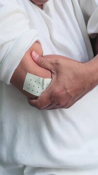 elderly asian man hand touching, holding the injured hand that wear a pain relief patch on the elbow for pain of tennis elbow symptom, hand movement shot, vertical video