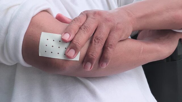 elderly asian man hand touching, holding the injured hand that wear a pain relief patch on the elbow for pain of tennis elbow symptom, hand movement shot, quarter view shot