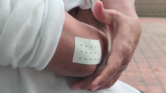 elderly asian man hand touching, holding the injured hand that wear a pain relief patch on the elbow for pain of tennis elbow symptom, hand movement shot, side angle profile view of body parts