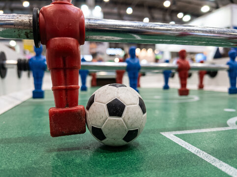 red player figure of table football holds the ball on the green playing field next to other blue and red figures conveying the excitement and atmosphere of a dynamic tabletop match