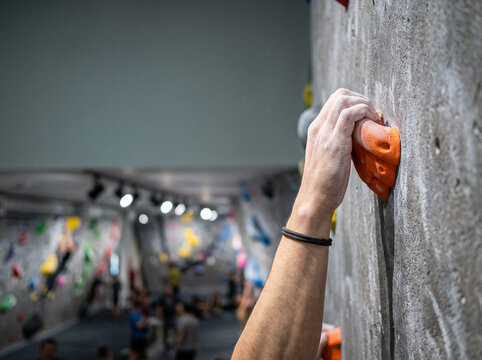 strong male hand in chalk holds tightly onto an orange hold on an artificial climbing wall close up demonstrating endurance grip and preparation for overcoming the route