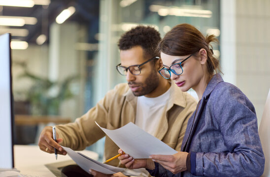 Analysts coworkers in office discussion reading documents. They compare charts, take notes, and plan for a finance report, focusing on data and teamwork. Clear planning and collaboration concept.