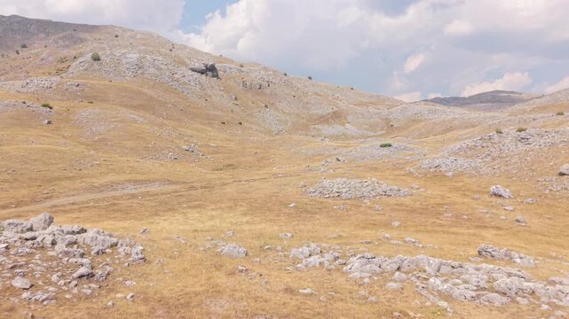 Drone Aerial View of Arid Mountain Landscape with Dry Yellow Grass, Rocky Hills and Clouds in Summer