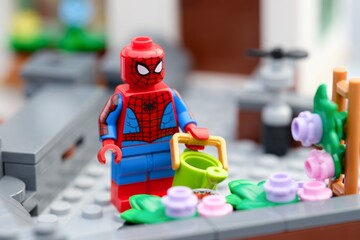 Naklejka premium Tambov, Russian Federation - August 23, 2026 A Lego Spiderman minifigure with a watering can next to a flower bed on a rooftop garden.