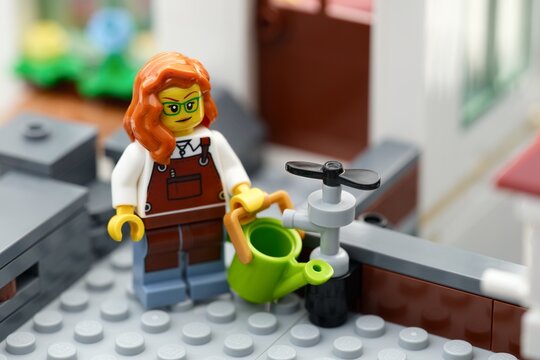 Tambov, Russian Federation - August 22, 2026 A Lego woman gardener minifigure with a green watering can next to a water tap.