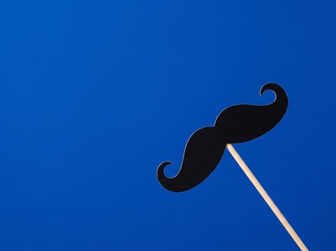Black paper mustache prop on a stick against a bright blue background