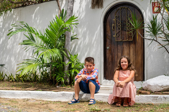 dos hermanos amigos ni&ntilde;os felices sentados fuera de una casa en una calle empedrada disfrutando afuera de una puerta de la casa de playa en el mar en sus vacaciones en un hermoso dia soleado