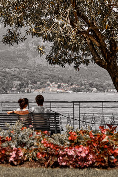 Bellagio, Lombardy, Como Lake, Italy. Couple in love sitting on the bench and watching the beauti. Famous Italian village and popular European travel destination. Summer scenery of como lake old town.