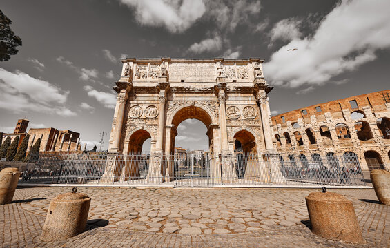 Triumphal Arch in ancient Rome Italy. Ancient vintage landmark. Famous monument near roman coliseum. Summer area with green trees and tourists people. Sunny day with blue sky and clouds.