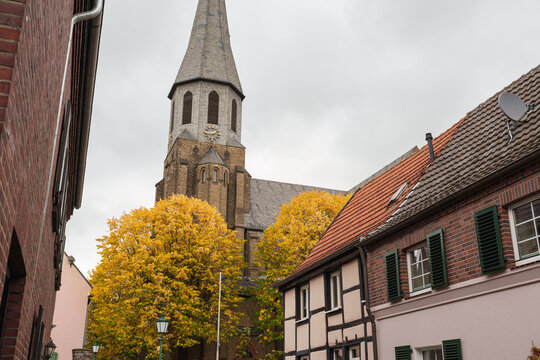 A St. Martinus church tower rises above historic houses and golden autumn trees in Zons, Germany