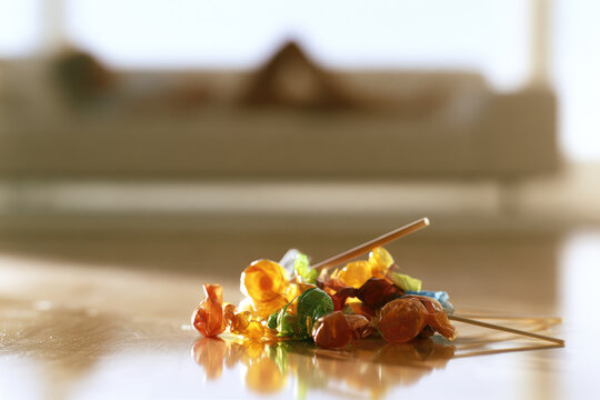 Colorful lollipop candy wrapper pile on polished floor with blurred sofa background and bright daylight creating reflection and waste concept